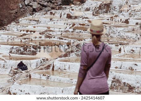 Tourist woman at Salineras de Maras, salt pan mine evaporation with white terrace ponds and agriculture extraction, old landmark attraction in Urubamba sacred valley near Cusco in Peru, South America.