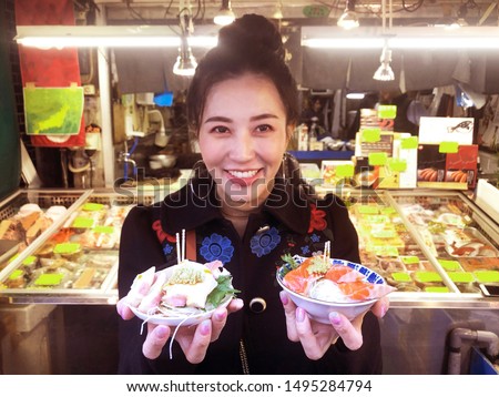Tourist woman showing salmon sashimi most popular delicious food in street food tsukiji fish market, Japan