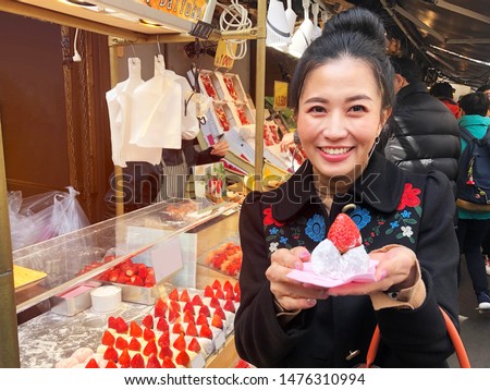 Tourist woman showing street food strawberry Daifuku, Strawberry Mochi at Tsukiji Fish Market in Tokyo.

