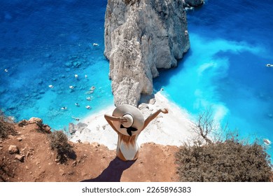 A tourist woman sits at the viewpoint of Keri and enjoys the view of the famous Mizithres rocks with turquoise sea at Zakynthos island, Greece