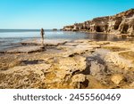 Tourist woman stand on rocky formations by sea cave in Ayia Napa, Cyprus. A shot from the inside of a sea cave in sunny Mediterranean coast of greek Cyprus. Grotto sea cave swim