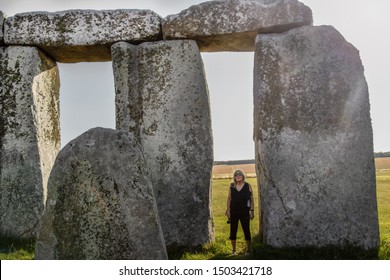 Tourist woman standing between stones at Stonehenge in England on sunny day to show how big they are