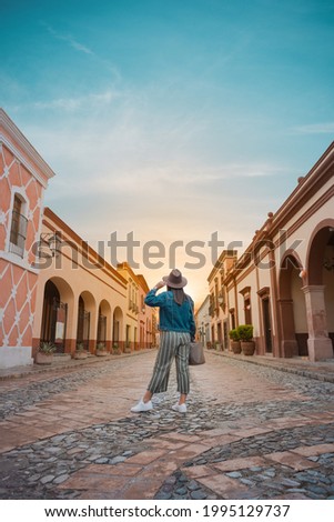 Tourist woman standing in the middle of the street of a magical town, town of La Peña del Bernal in Querétaro, Mexico, with sunset in front, summer day