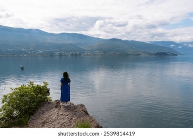 Tourist woman standing on edge of rock formation with panoramic morning views of Lake Ohrid, North Macedonia. Calm water surface reflecting surrounding hills and mountains. Summer travel destination - Powered by Shutterstock