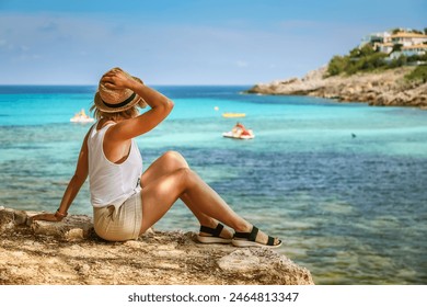 Tourist woman in straw hat, positioned by the shore, gazing at the clear blue waters, representing the Mallorca travel experience - Powered by Shutterstock