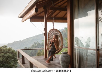 Tourist Woman Swing On Wicker Rattan Hang Chair In The Jungle, Nature Mountains View, Hold In Hands Cup Of Tea/coffee