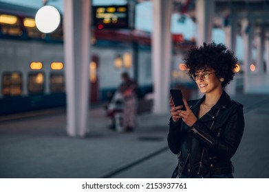 Tourist Woman Texting Message And Plan Route Of Stop Railway And Railroad Transport In The Night. Enjoying Travel Concept. Girl Texting On Smartphone While At The Train Station.