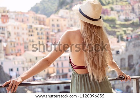 Tourist woman traveling, looking at the view. Beautiful place in Italy. Girl in summer hat enjoying sunny travel vacation in Europe. Back view of happy blonde girl .