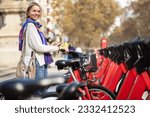 Tourist Woman using red bicycle in a bike rental station in the city with travel sharing app 