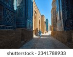 Tourist woman walking in Beautiful Historical cemetery of Shahi Zinda entry Gate with finely decorated by blue and turquoise stone mosaic mausoleums in Samarkand, Uzbekistan.