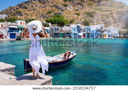 A tourist woman in a white dress and hat looks at the colorful fishing village of Klima on the island of Milos, Cyclades, Greece, during summer time Imagine de stoc © 