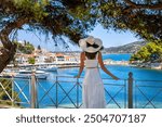 A tourist woman in a white summer dress looks at the harbour of Skiathos Town, Sporades, Greece