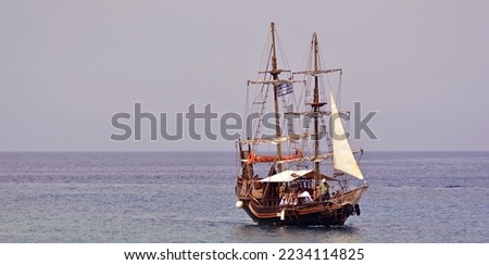 Tourist wooden pirate ship goes by sea from the bay of the island with tourists. Wooden masts and white sails are visible on the ship.