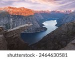 A tourist in a yellow jacket stands on the edge of the Troll