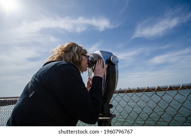 Tourist Young Adult Woman Looks Through A Viewfinder Binoculars Out Into The Ocean