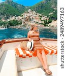 Tourist young woman lounges in orange dress relaxing on vacation on boat in the ocean located in the Amalfi Coast, Positano, Italy, summer lifestyle concept