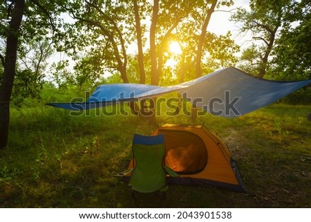 touristic tent under a tarp in forest at the sunset, summer camping scene