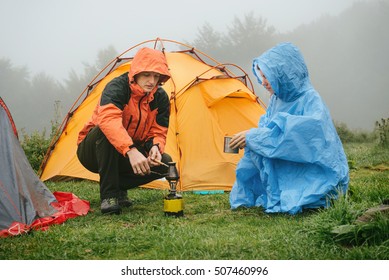 Tourists cooking coffee on primus near the tent in the mountains. Foggy and rainy camping while hiking. 