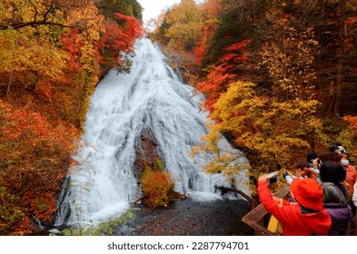Tourists crowding on a viewpoint to take photos of beautiful Yudaki Waterfall 湯滝 and the brilliant fall colors on the cliffs in autumn season, in Nikko National Park 日光国立公園, Tochigi Prefecture, Japan