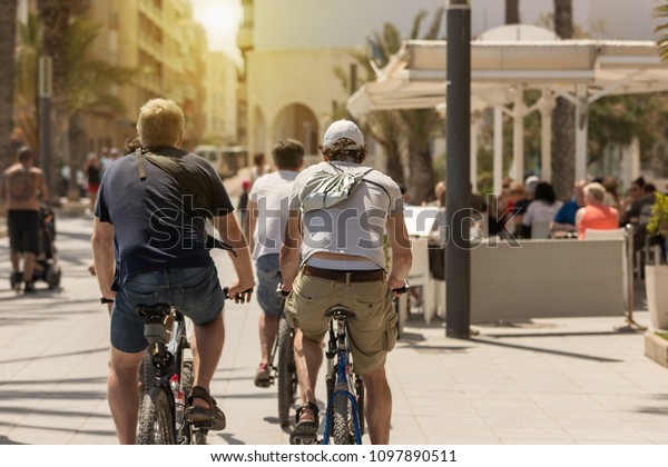 Tourists cycling on a\
pleasant and sunny summer afternoon through the streets of Europe\
between bars and restaurants. People on bike on crowded sidewalks\
going slowly.