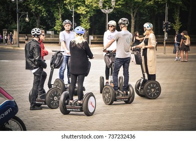 Tourists Gathered For A Segway Tour In Front Of The Eastern Side Of The Berlin Wall. Behind Them Is The Park With Many Monuments From World War 2. Summer 25. August 2017.