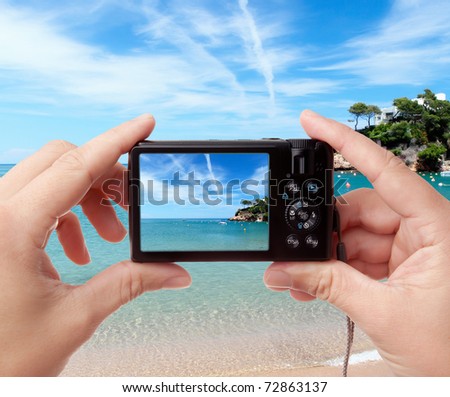 Tourist's hands holding digital photo camera on vacations, taking picture of beautiful sunny seaside