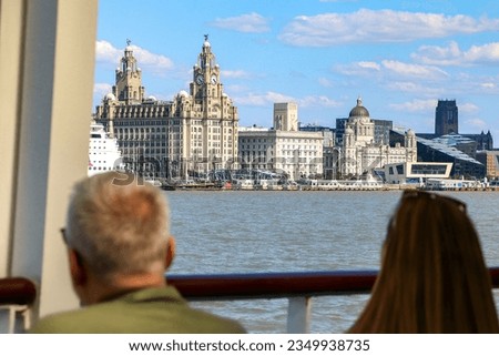 Tourists on Mersey ferry River cruise looking out into iconic Liverpool skyline view of the Three Graces - the Royal Liver Building, the Cunard Building and the Port of Liverpool Building