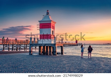 Tourists on the shore of Lignano Sabbiadoro resort. Splendid outdoor scene of Adriatic coast of Italy with lighthous and old wooden pier. Picturesque morning seascape of Mediterranean sea.
