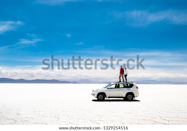 Tourists on white car rooftop in spacious sunshine\
Salar de Uyuni