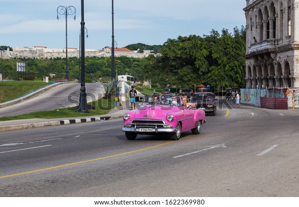 Tourists in a pink\
convertible classical car travel on the highway in Havana, Cuba in\
November 2015.