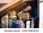 Tourists putting travel bag into travel bus at city street. Bus passengers putting luggage into the trunk when the bus stopped at terminal. Pack luggage and board the sightseeing bus. Happy journey.