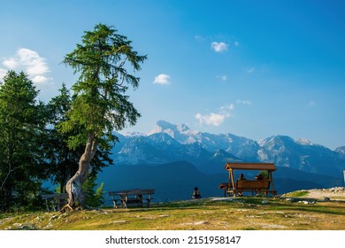 Tourists resting on the top of Vogel mountain above famous Bohinj lake. Scenic panorama of Julian Alps. Triglav summit - highest mountain in Slovenia - in the center. Slovenia
