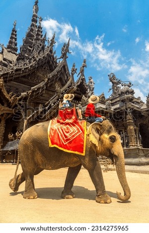 Tourists ride elephant around the Sanctuary of Truth in Pattaya, Thailand in a summer day