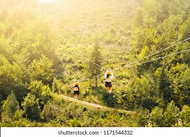 Tourists ride on the Zipline over the forest. Two women in helmets sliding on a zip line in an adventure park. Couple in helmets hanging on a rope way. - Powered by Shutterstock