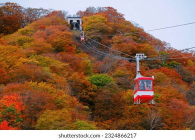 Tourists riding in cable cars of Akechidaira Ropeway up to a viewing platform to enjoy the panorama of mountains blanketed with vibrant fall colors, in Nikko National Park, Tochigi, Japan