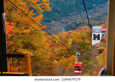 Tourists riding in the gondolas of Akechidaira 明智平 Ropeway up to a lookout platform to enjoy the panoramic view of mountains blanketed with vibrant fall colors, in Nikko National Park, Tochigi, Japan