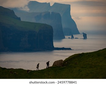 Tourists silhouettes on background of Risin og Kellingin rocks and cliffs of Eysturoy and Streymoy Islands seen view point near Kallur lighthouse on the Kalsoy Island. Faroe Islands, Denmark. - Powered by Shutterstock