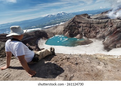 Tourists sits in apex of crater of active volcano and relaxes watching at beautiful volcanic landscape of Kamchatka on sunny day. Gorely Volcano, Kamchatka Peninsula, Russian Far East - July 21, 2013