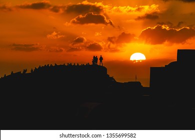 tourists stand atop a castle to watch the sun set at Santorini, Greece