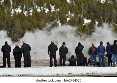 Tourists stand on a misty boardwalk in Yellowstone National Park, awaiting the eruption of Old Faithful geyser.