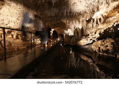 Tourists Take In The Stalactites That Hang Dramatically From The Roof Of Lake Cave In Margaret River, Western Australia. Motion Blur Of People Due To Long Exposure.