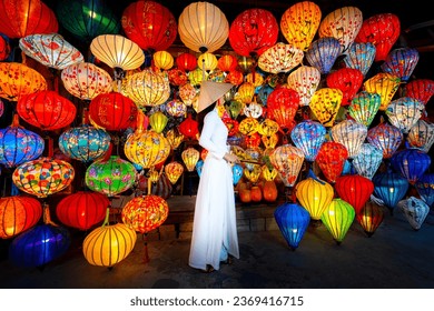 Tourists in traditional Vietnamese clothing look at paper lanterns in Hoi An ancient town. Traditional Vietnamese culture and lanterns at Hoi An ancient city Vietnam - Powered by Shutterstock