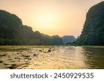 Tourists traveling in boats along the Ngo Dong River at the Tam Coc portion, Ninh Binh Province, Vietnam. Rowers using their feet to propel oars. Landscape formed by karst towers and rice fields