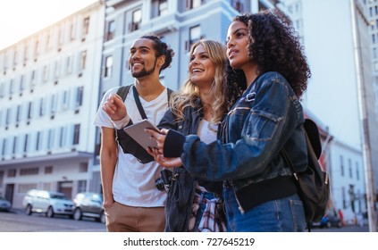 Tourists Using Navigation Tools To Explore The City. Man With Two Women Friends Exploring The City With Travel Accessories.