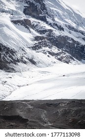 Tourists Walk A Trail Leading To The Terminus Of Athabasca Glacier, Along The Icefields Parkway Of Jasper National Park. In The Distance, A Tour Vehicle Can Be Seen Driving Onto The Ice.