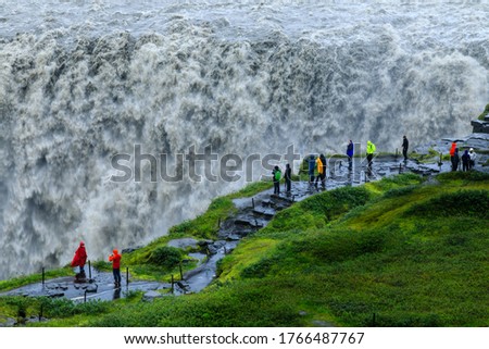 Tourists at a wet and powerful  Dettifoss waterfall as it gushes into Jökulsárgljúfur canyon, with rising mist and spray and green Summer grasses, Vatnajökull National Park, North Iceland, Europe