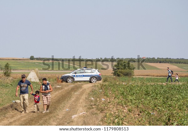 TOVARNIK, CROATIA - SEPTEMBER 19, 2015: Group of\
refugees, passing in front of a Croatian police car while crossing\
Serbia Croatia border in Tovarnik Sid on the Balkans Route, during\
Refugee Crisis