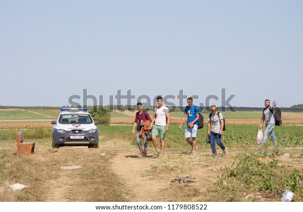 TOVARNIK, CROATIA - SEPTEMBER 19, 2015: Group of
refugees, passing in front of a Croatian police car while crossing
Serbia Croatia border in Tovarnik Sid on the Balkans Route, during
Refugee Crisis