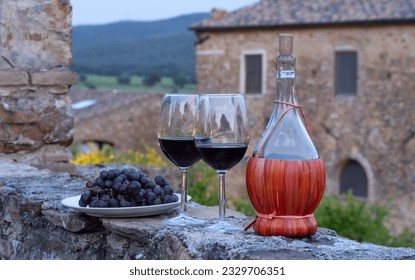 Tow glasses of red wine and typical chianti wine bottle Fiasco against the backdrop of the Tuscany landscape