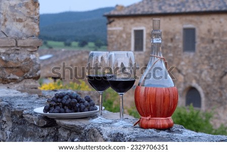 Tow glasses of red wine and typical chianti wine bottle Fiasco against the backdrop of the Tuscany landscape
